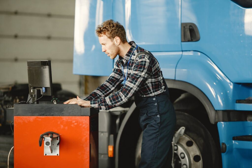 A mechanic focuses on a computer to diagnose and repair a large truck in a workshop.