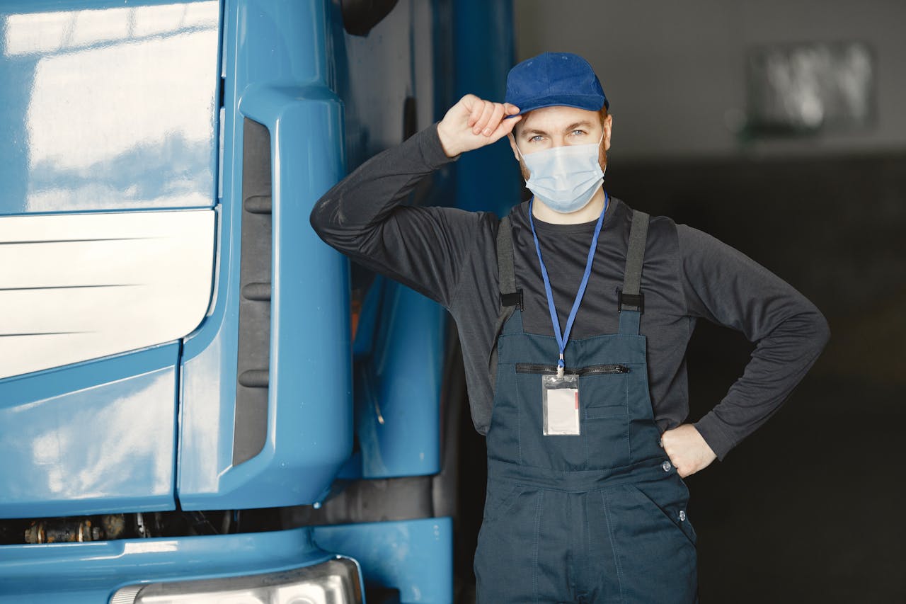 our-journey-01 Mechanic in overalls and mask by blue truck in garage setting.