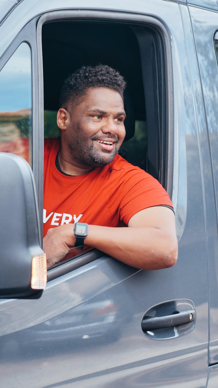 who-we-are Happy delivery driver in red shirt smiling out van window, creating a positive delivery service vibe.
